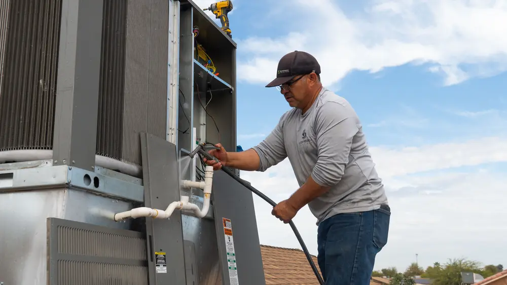 EcoEnergy Solutions technician washing the condenser coils during an AC tune-up in Yuma, AZ