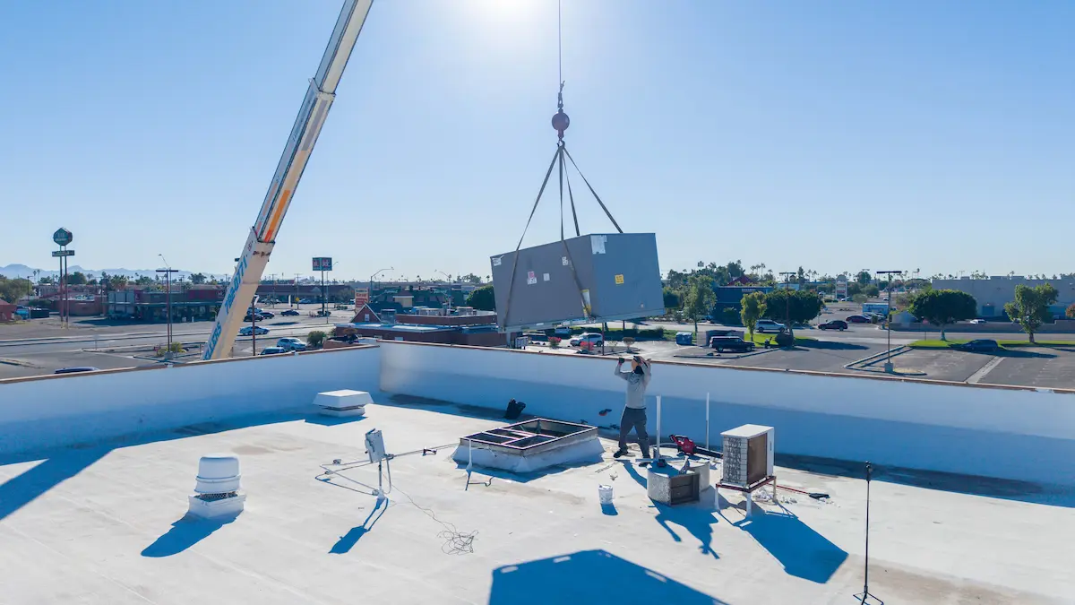 EcoEnergy Solutions technician guiding a new rooftop AC package unit into place with a crane in Yuma, AZ