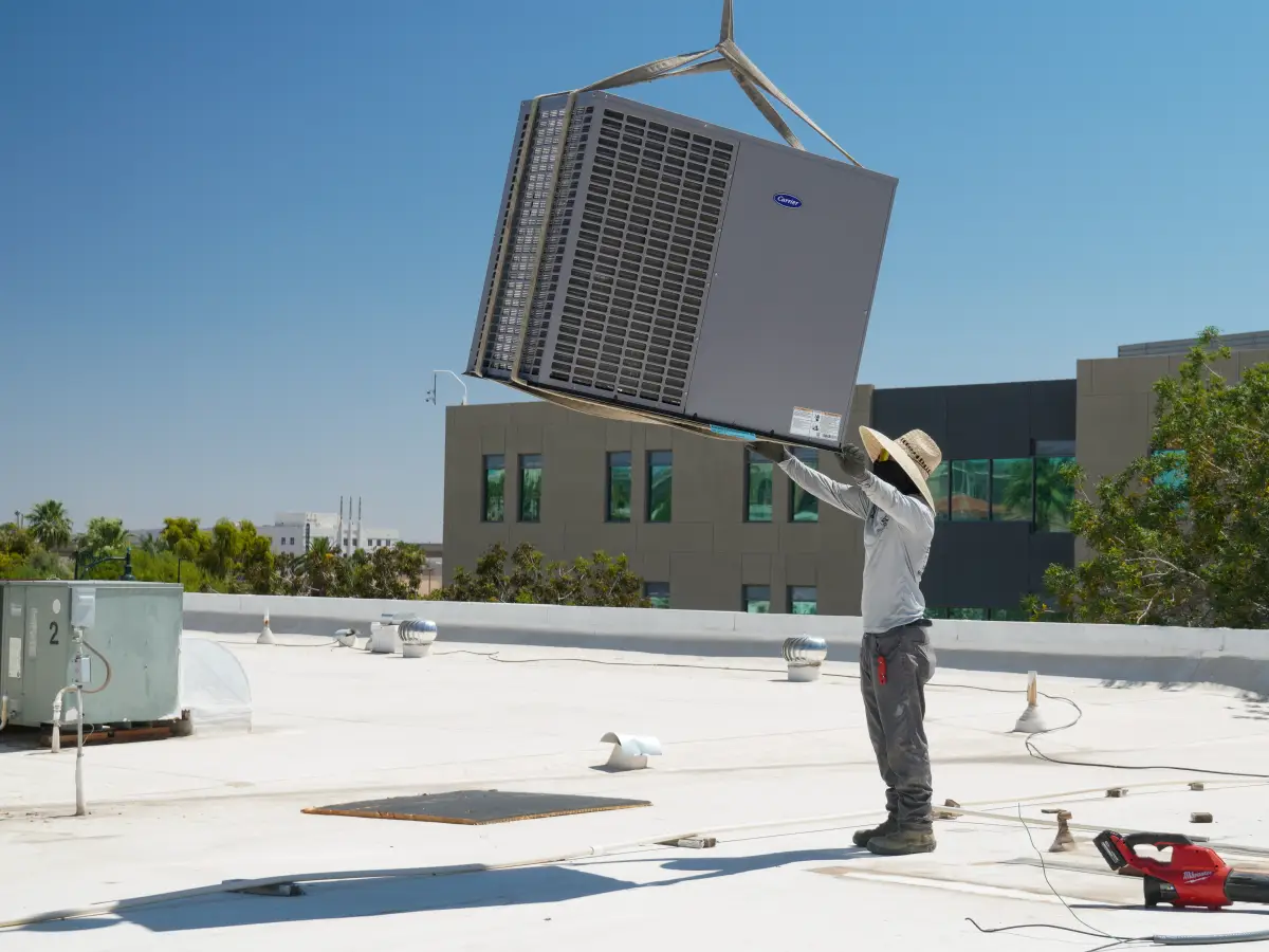 Carrier packaged rooftop unit installation in Yuma, AZ by EcoEnergy Solutions EcoEnergy Solutions technician guiding a Carrier packaged rooftop unit into place in Yuma, AZ