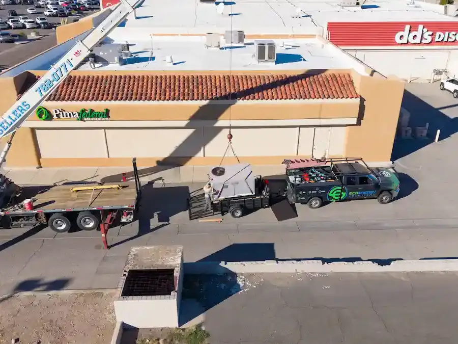 Crane lifting a rooftop AC unit onto a Yuma, AZ commercial building beside the EcoEnergy Solutions truck