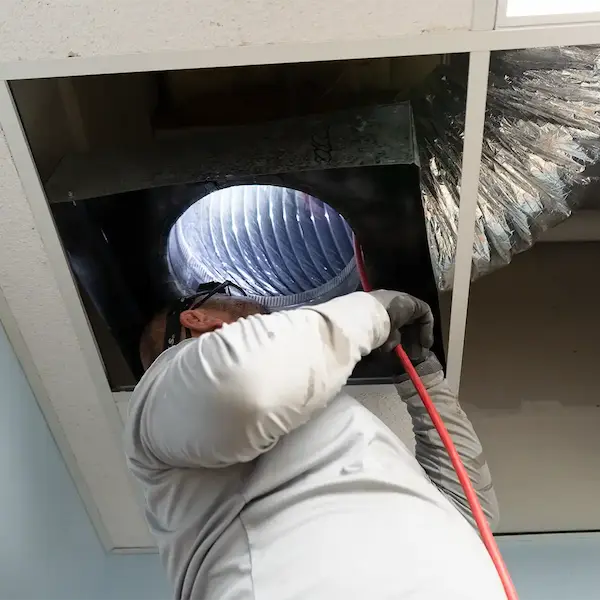 Technician inspecting an air duct system from the ceiling