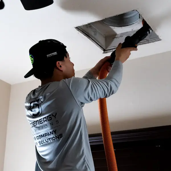 Professional cleaning a ceiling air vent with a vacuum