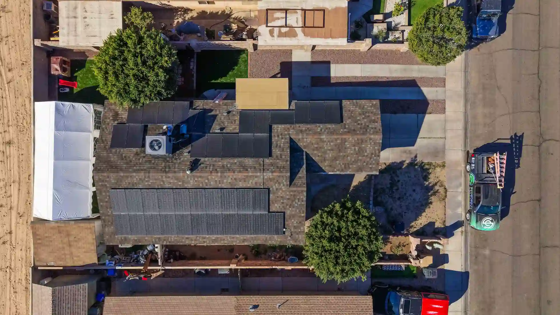 Aerial view of a Yuma home with a new shingle roof, rooftop solar panels and an EcoEnergy technician servicing the AC unit