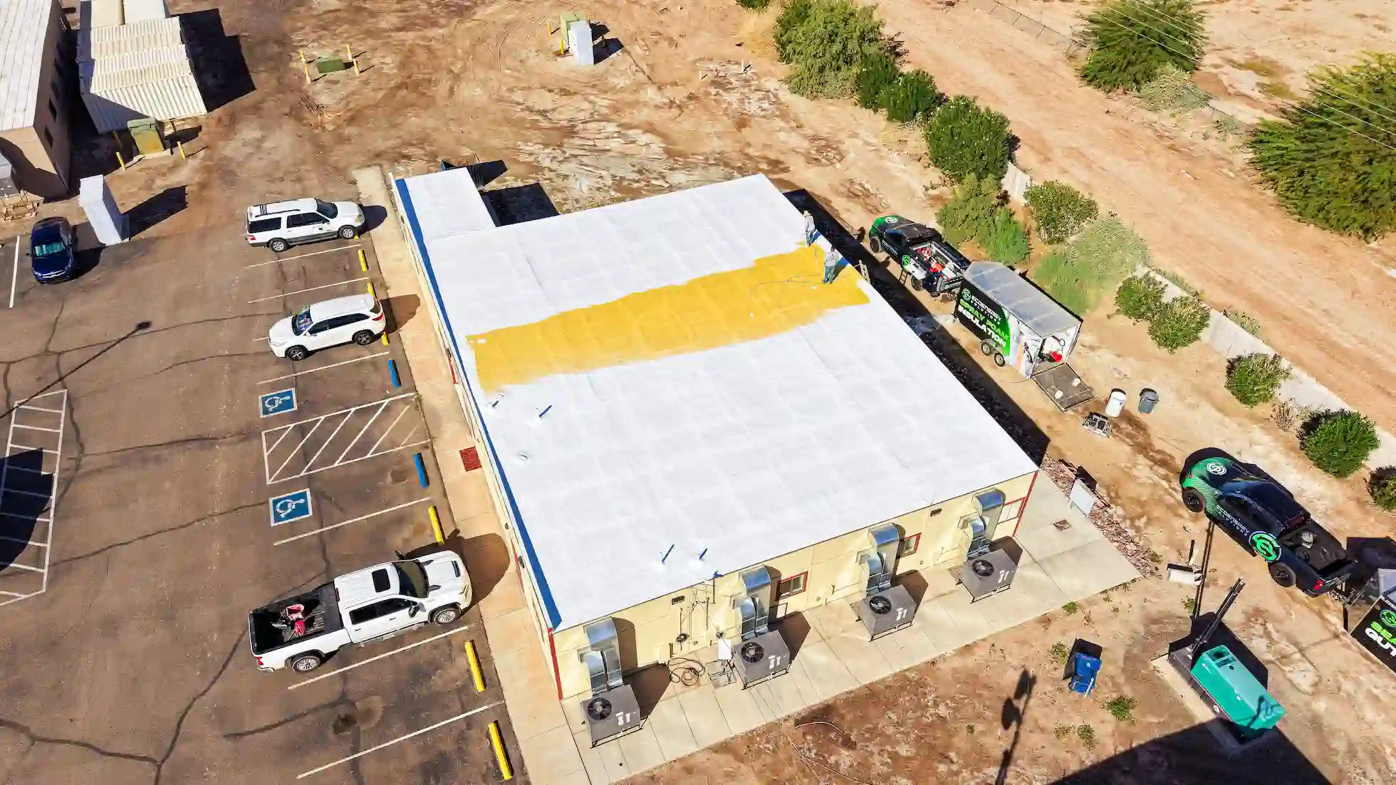 EcoEnergy crew spraying foam insulation over a commercial roof in Yuma, AZ, with the company spray foam trailer parked alongside